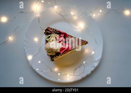 Ein Stück hausgemachter Schokoladenkuchen auf einem weißen Teller inmitten von Lichtern. Ansicht f Stockfoto