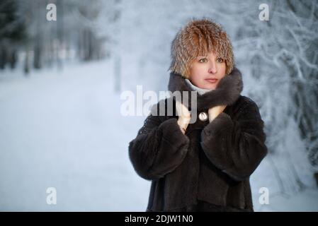 Attraktive Frau mittleren Alters gekleidet in Winterkleidung Pelz Mantel und hut im Winterwald Stockfoto