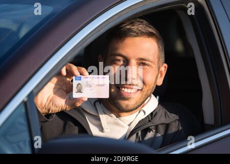 Attraktiver lächelnder junger Mann zeigt stolz seinen Führerschein Des Autofensters Stockfoto