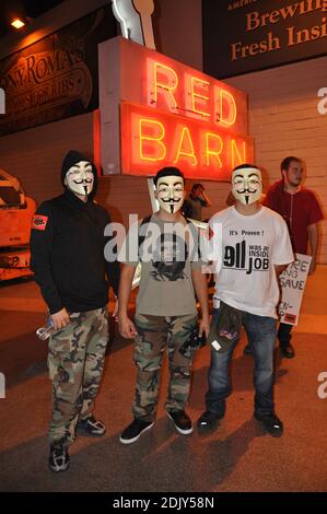 Drei männliche Demonstranten in der Occupy Las Vegas Bewegung, die Guy Fawkes Masken tragen, posieren vor einem Neonschild, das die Red Barn wirbt. Stockfoto