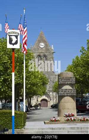 Ein Denkmal für die Lufttruppen, die Sainte-Mere-Eglise befreit, berühmt für einen Fallschirmjäger auf dem Kirchturm gefangen (hinten) Normandie, Frankreich. Stockfoto