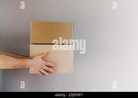 Die Hände des Lieferdienstmanns halten Kartons auf dem grauen Hintergrund. Lieferservice, Online-Shopping und Logistikkonzept. Stockfoto