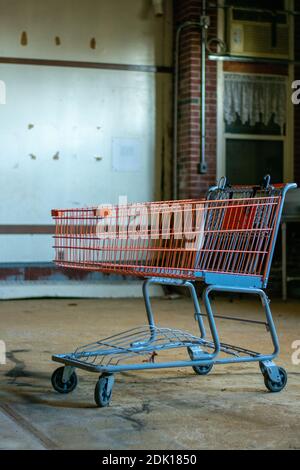 Ein roter Einkaufswagen in einem großen leeren Raum in Ein zerstörtes verlassene Gebäude Stockfoto