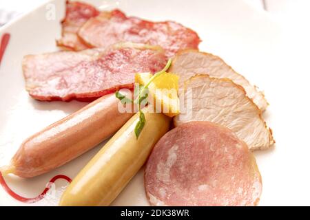 Ein Blick von oben Nahaufnahme von verschiedenen Arten von Schinken und Würste auf einem weißen Teller mit einer Scheibe Orange Stockfoto