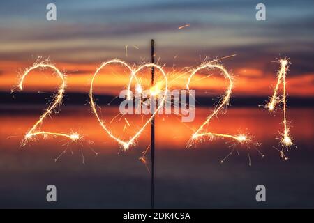 2021 geschrieben mit Sparkle Feuerwerk auf Sonnenuntergang Hintergrund, glückliches neues Jahr 2021 Konzept. Stockfoto