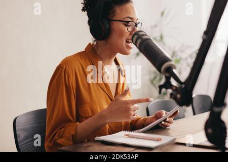 Weibliche Podcasterin, die ihren Podcast von zu Hause aus aufnahm und ausstrahlte. Frau, die von zu Hause aus einen Notizblock liest und in ein Mikrofon spricht. Stockfoto