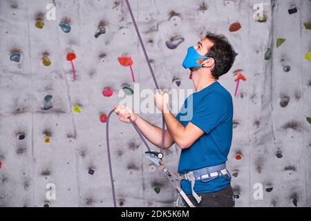 Männliche Kletterer trägt eine schützende Gesichtsmaske, die einen anderen Kletterer sichert. Seilsicherung Klettergurt. Neuer Normalwert. Stockfoto