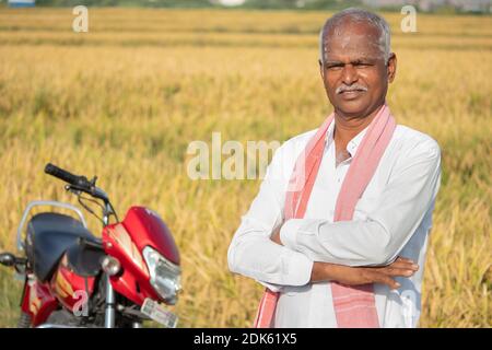 Happy Indian Farmer mit gekreuzten Armen stehen mit Fahrrad vor Der Landwirtschaft Ackerland - Konzept der guten Ernteertrag Und Landwirt Fahrrad Darlehen Stockfoto