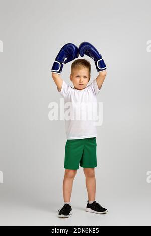 Kleiner Boxkämpfer Junge in blauen Boxerhandschuhen ist gestikulierende Sieg. Kind träumt davon, ein Boxchampion zu werden Stockfoto