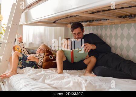 Vater mit Söhnen, die Buch auf dem Bett lesen Stockfoto