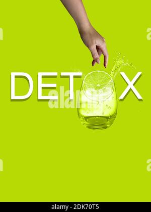 Weißer Detox-Text auf grünem Hintergrund isoliert. Weibliche Hand werfen Stück Zitrone zu Glas Wasser. Horizontale Aufnahme. Speicherplatz kopieren. Stockfoto