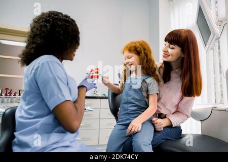 Weibliche afrikanische Arzt demonstriert richtige Zahnpflege für junge Mutter und Schulmädchen Kind. Glückliches Kind putzen Zähne mit Zahnbürste und Spaß haben Stockfoto