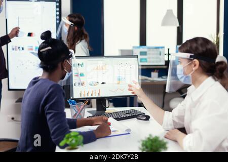 Der Manager zeigt den finanzbericht afrikanischer Kunden mit Gesichtsmaske gegen Covid19. Multiethnisches Team arbeitet in Unternehmen mit neuen normalen Respekt soziale Distanz während der globalen Pandemie mit Coronavirus. Stockfoto