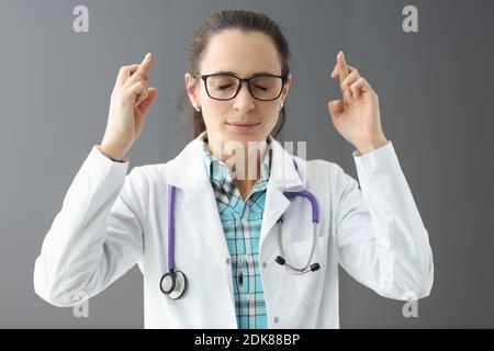 Ärztin mit geschlossenen Augen hält gekreuzte Finger Stockfoto