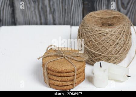 Lebkuchenkekse mit Garn gebunden. In der Nähe befinden sich Kerzenstutzen und ein Garnstrang. Auf Brettern weiß lackiert. Stockfoto