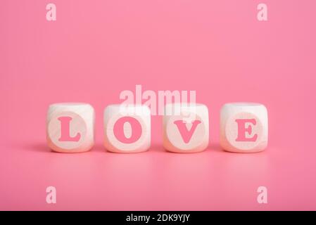 Text Holzblöcke Schreibweise des Wortes Liebe auf rosa Hintergrund. Das Konzept der ewigen Liebe und des Glücks. Stockfoto