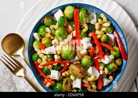 Makkaroni-Salat mit Brokkoli-Sprossen, Paprika-Streifen, Feta und Erdnuss in einer Schüssel mit Erdnusssauce auf einem Marmortisch, horizontale Ansicht von oben, f Stockfoto