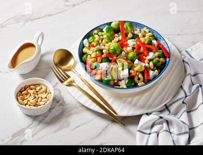 Makkaroni-Salat mit Brokkoli-Sprossen, Paprika-Streifen, Feta und Erdnuss in einer Schüssel mit Erdnusssauce auf einem Marmortisch, horizontale Ansicht von oben Stockfoto