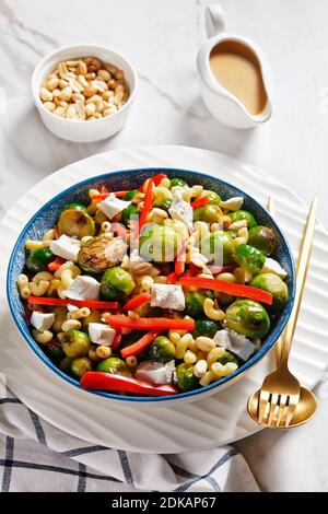 Makkaroni-Salat mit Brokkoli-Sprossen, Paprika-Streifen, Feta und Erdnuss in einer Schüssel mit Erdnusssauce auf einem Marmortisch, vertikale Ansicht von oben, Klo Stockfoto