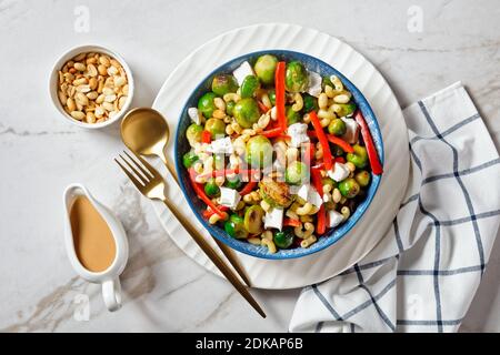 Makkaroni-Salat mit Brokkoli-Sprossen, Paprika-Streifen, Feta und Erdnuss in einer Schüssel mit Erdnusssauce auf einem Marmortisch, horizontale Ansicht von oben, f Stockfoto