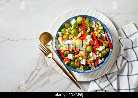 Makkaroni-Salat mit Brokkoli-Sprossen, Paprika-Streifen, Feta und Erdnuss in einer Schüssel mit Erdnusssauce auf einem Marmortisch, horizontale Ansicht von oben, f Stockfoto