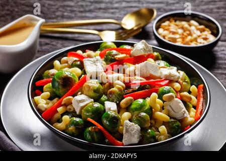 Makkaroni-Salat mit Brokkoli-Sprossen, Paprika-Streifen, Feta und Erdnuss in einer schwarzen Schüssel mit Erdnusssauce auf einem Holztisch, horizontale Ansicht von ab Stockfoto