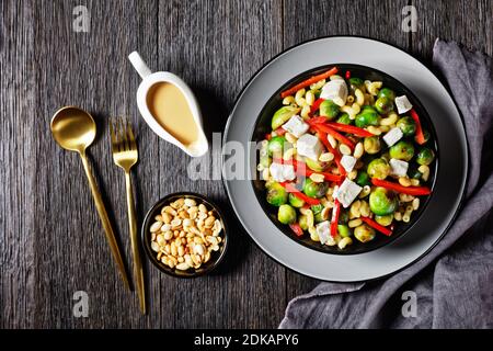 Makkaroni-Salat mit Brokkoli-Sprossen, Paprika-Streifen, Feta und Erdnuss in einer schwarzen Schüssel mit Erdnusssauce auf einem Holztisch, horizontale Ansicht von ab Stockfoto