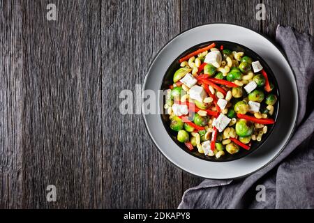 Makkaroni-Salat mit Brokkoli-Sprossen, Paprika-Streifen, Feta und Erdnuss in einer schwarzen Schüssel mit Erdnusssauce auf einem Holztisch, horizontale Ansicht von ab Stockfoto