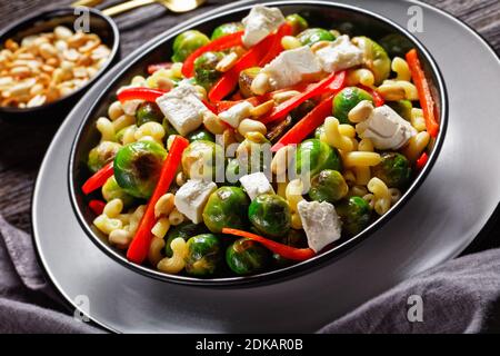 Makkaroni-Salat mit Brokkoli-Sprossen, Paprika-Streifen, Feta und Erdnuss in einer schwarzen Schüssel mit Erdnusssauce auf einem Holztisch, horizontale Ansicht von ab Stockfoto