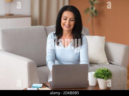 Reife Frau sitzt auf dem Sofa und arbeitet am Computer Stockfoto