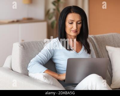 Reife Frau sitzt auf der Couch und arbeitet am Computer Stockfoto