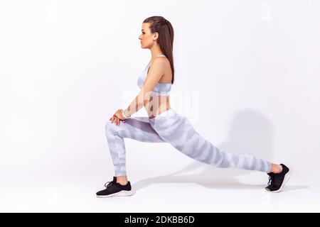 Profil Porträt in voller Länge athletische Frau in weißer Sportbekleidung tun Unterkörper Sport Übung, Strecken Beine, Aufwärmen Muskeln für Flexibilität. Stockfoto