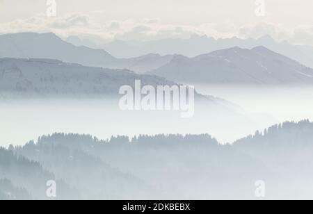 Schnee Berge im niedrig liegenden Inversion Tal Nebel. Silhouetten von nebligen Bergen und Bäumen. Landschaftlich schöne verschneite Winterlandschaft. Blick von Stuiben Swiss Stockfoto