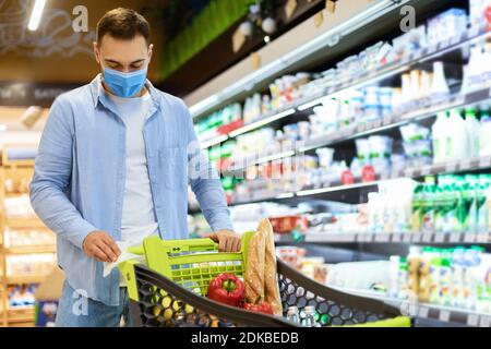 Junger Mann in Maske Reinigung Griff des Warenkorbs Stockfoto