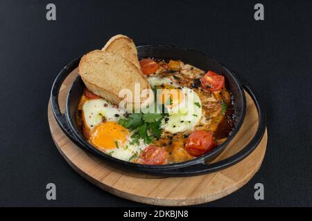 Gesundes Frühstück shakshuka - Spiegeleier, Zwiebel, Paprika, Tomaten und Gewürze in Gusseisen Steppan auf alten Holzbrett. Stockfoto