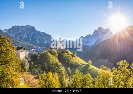 Ein klassischer Blick auf das Dorf Colle Santa Lucia dominiert von der Pfarrkirche und Monte Pelmo im Hintergrund, Herbstszene mit der Sonne am Himmel, Agordino, Provinz Belluno, Venetien, Italien, Europa Stockfoto