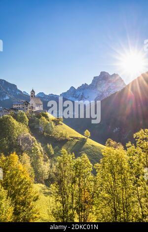 Ein klassischer Blick auf das Dorf Colle Santa Lucia dominiert von der Pfarrkirche und Monte Pelmo im Hintergrund, Herbstszene mit der Sonne am Himmel, Agordino, Provinz Belluno, Venetien, Italien, Europa Stockfoto