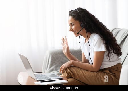 Glückliche junge Frau mit dem Headset winkt auf Laptop-Bildschirm Stockfoto