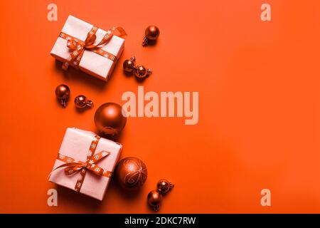 Kreative holdiay Hintergrund mit Geschenken, in rotem Papier mit rotem Band Schleife und Weihnachtskugeln auf orangefarbenem Hintergrund gewickelt. Frohe Weihnachten und ein glückliches neues Jahr Urlaub Hintergrund. Flach liegend, Draufsicht, Rahmen. Stockfoto