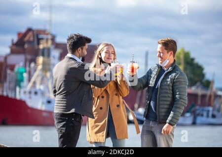 Zwei Männer und eine Frau mit Alltagsmasken in der Corona-Zeit, in der kalten Jahreszeit unterwegs in der Stadt, Drinks im Freien, kleines Treffen unter Bekannten, Stockfoto