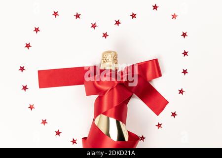 Eine Geschenkflasche Champagner in goldener Folie eingehüllt Ein rotes Seidenband und verstreute Konfetti auf einem weißen Hintergrund Stockfoto