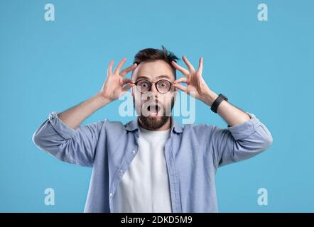 Unglaubliches Angebot. Erstaunt kaukasischen Kerl in lässigen Outfit und Brille Öffnung Mund in Überraschung auf blauem Hintergrund Stockfoto