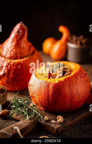 Tasty baked pumpkin stuffed with rice, vegetables, cashews and dried fruits on wooden table with dark background Stockfoto