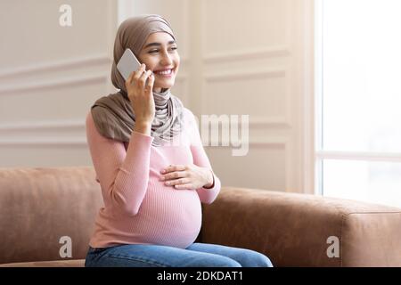 Schwangere Muslimische Dame In Hijab Gespräch Am Telefon Zu Hause Stockfoto