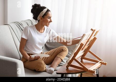 Inspirierte junge Frau auf der Couch sitzen und malen Stockfoto