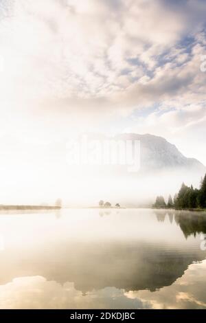 Herbststimmung an einem kleinen See in den bayerischen Alpen, im Hintergrund das Karwendelgebirge, eine kleine Halbinsel im Nebel und die Spiegelung im Wasser. Die neblige Atmosphäre mit den zerklüfteten Bergen hat eine fast mystische Wirkung. Stockfoto