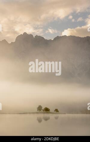 Herbststimmung an einem kleinen See in den bayerischen Alpen, im Hintergrund das Karwendelgebirge, eine kleine Halbinsel im Nebel und die Spiegelung im Wasser. Die neblige Atmosphäre mit den zerklüfteten Bergen hat eine fast mystische Wirkung. Stockfoto