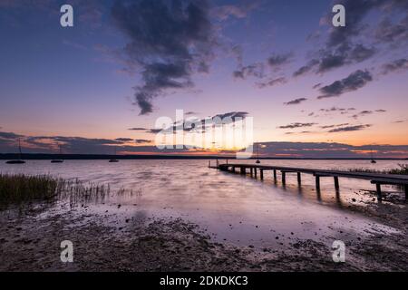 Abendstimmung auf einer der unzähligen Holzstege am Ammersee bei Wartaweil, im Hintergrund der Mondaufgang, Farben und individuell verankerte Segelboote. Stockfoto