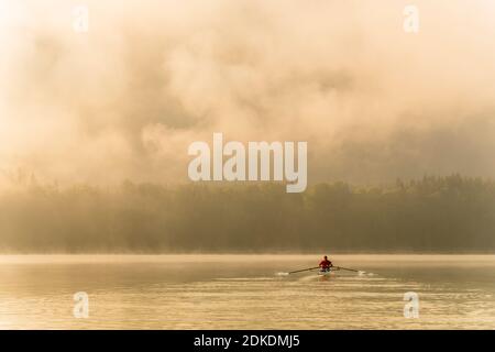 Kajakfahrer oder Rennfahrer genießen eine Fahrt auf dem Sylvensteinspeicher am frühen Morgen bei Sonnenaufgang, bei Nebel und leichter Stimmung. Stockfoto