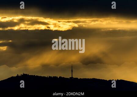 Stürmische Lichtstimmung auf dem Peißenberg bei Weilheim in den bayerischen Alpen. Der Fernsehturm ist schattig zu sehen und die Gemeinde links. Stockfoto